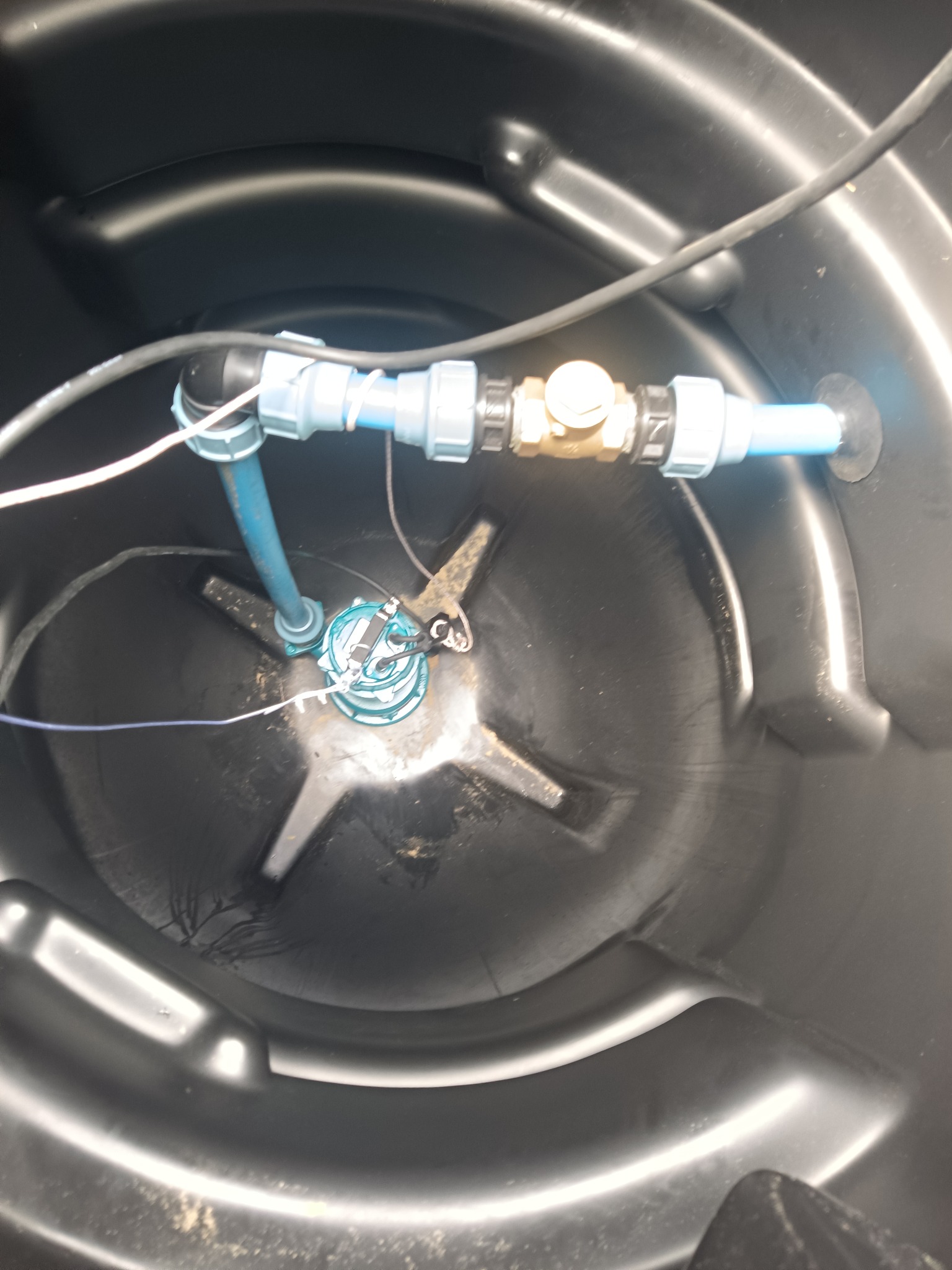 Wnętrze zbiornika z zainstalowaną pompą drenażową i rurami. Widoczne elementy instalacji wewnątrz czarnego zbiornika z tworzywa.