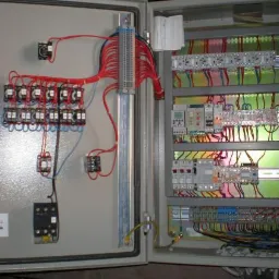 Otwarta szafa sterownicza z licznymi przekaźnikami, bezpiecznikami i przewodami, widoczne logo firmy Thermotechnik w lewym dolnym rogu.