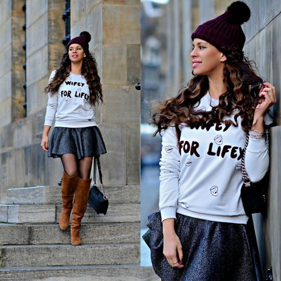 Kobieta w stylizacji z nadrukiem 'Wifey for Life' na szarej bluzie, czarnej mini spódniczce i brązowych kozakach, pozująca na schodach, z widocznym nadrukiem na bluzie i fakturą spódnicy.