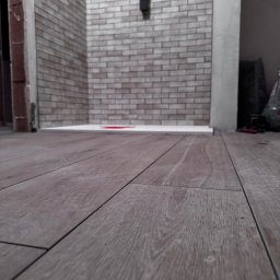 TK Format - Ułożone panele podłogowe w łazience z wykończoną ścianą z cegiełek. Widoczny fragment kabiny prysznicowej. Ujęcie z niskiej perspektywy.