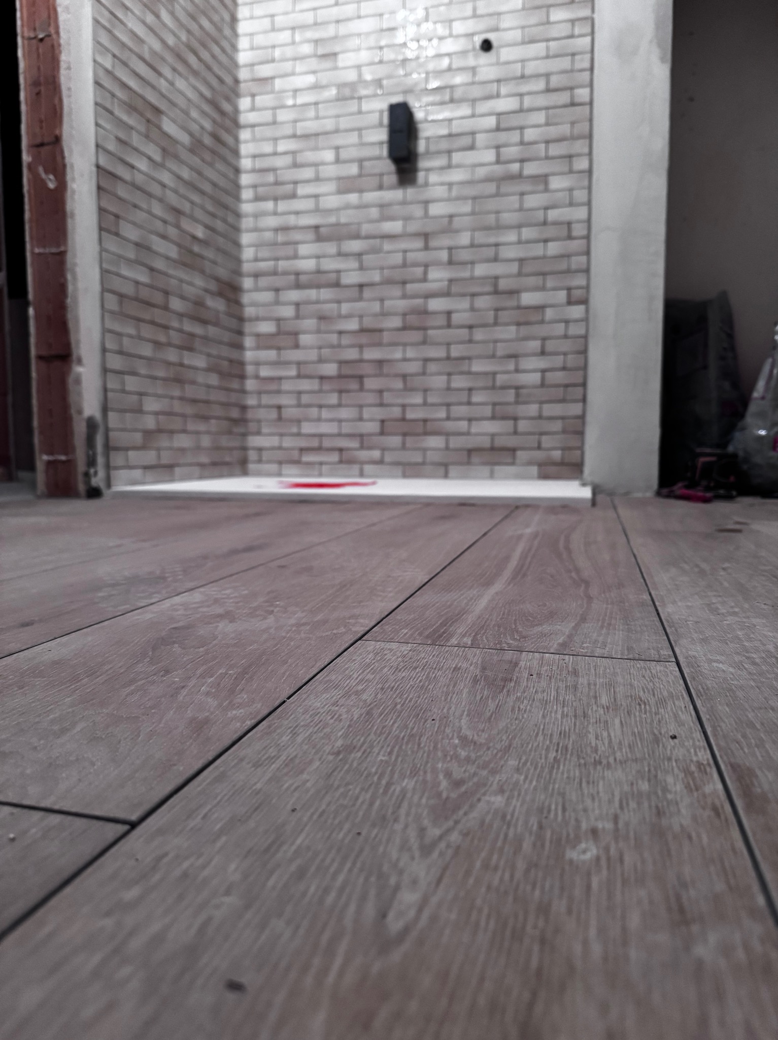 Ułożone panele podłogowe w łazience z wykończoną ścianą z cegiełek. Widoczny fragment kabiny prysznicowej. Ujęcie z niskiej perspektywy.