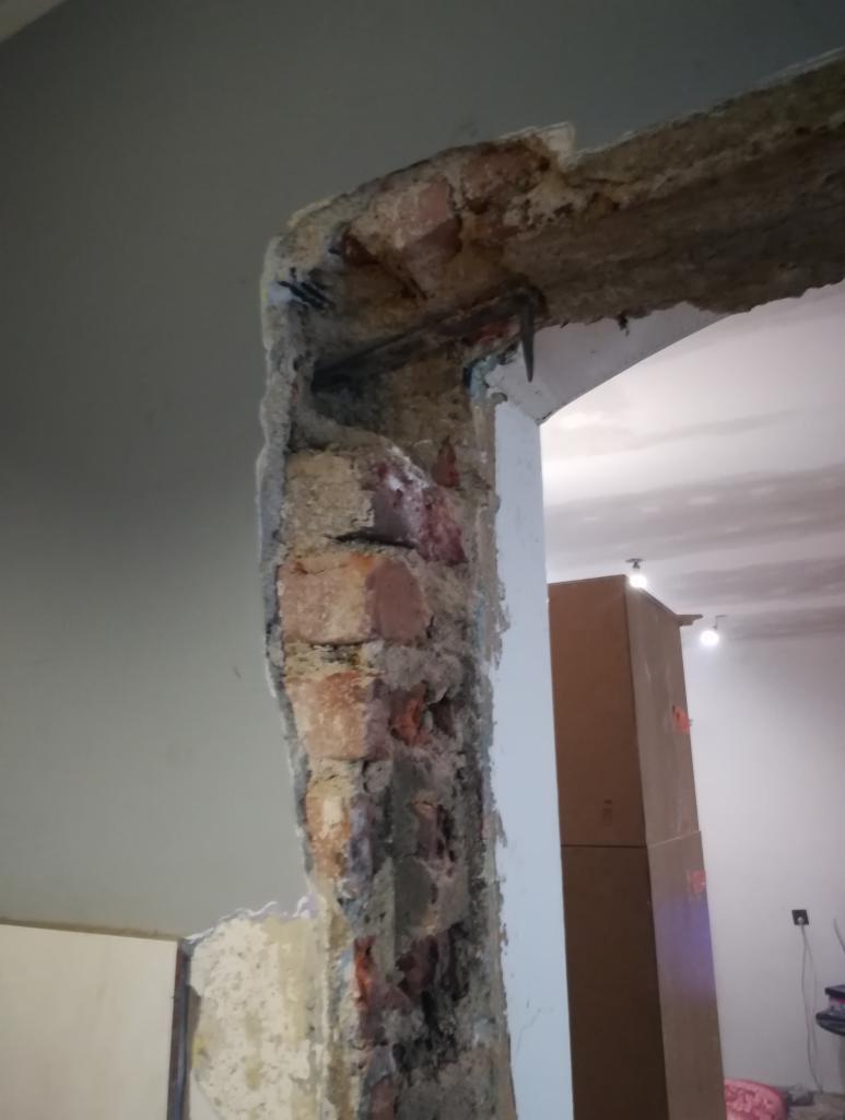 Fragment ściany z odsłoniętą czerwoną cegłą i wystającym zbrojeniem, w trakcie prac przygotowawczych do wykończenia wnętrza.