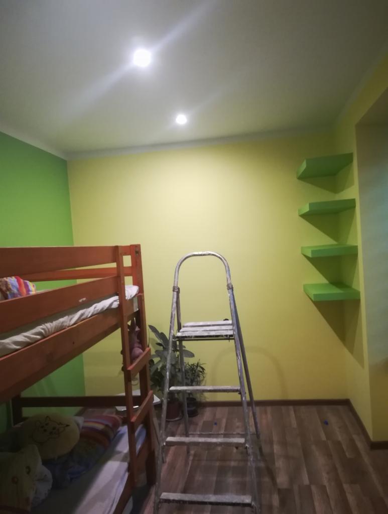 Pokój dziecięcy z łóżkiem piętrowym, ścianami w dwóch odcieniach zieleni i żółci oraz drabina malarska stojąca na drewnianej podłodze.