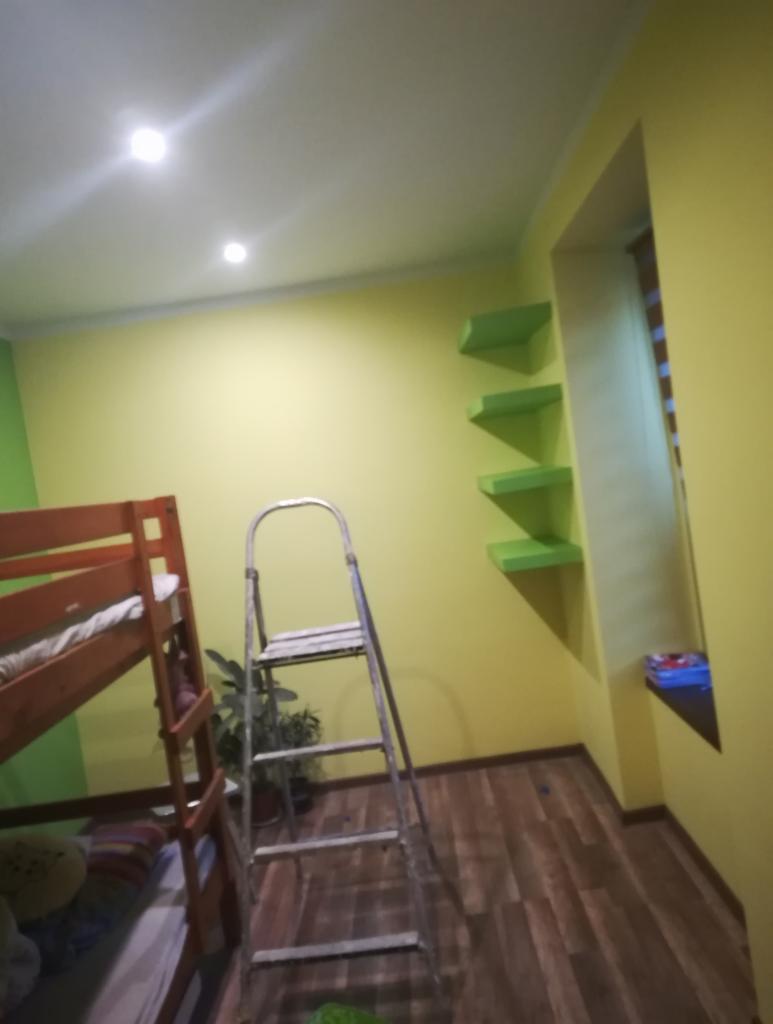 Pokój dziecięcy z łóżkiem piętrowym, ścianami w odcieniach żółci i zieleni, drewnianą podłogą oraz metalową drabiną w trakcie prac wykończeniowych.
