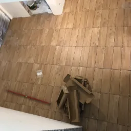 Układanie płytek imitujących drewno na podłodze w Olesnie, widoczne krzyżyki dystansowe, puste kartony po płytkach i poziomica.