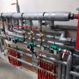 Rozbudowana instalacja grzewcza z licznymi zaworami, manometrami i pompami obiegowymi w Bieruniu, z widocznym czerwonym separatorem powietrza Flamco.