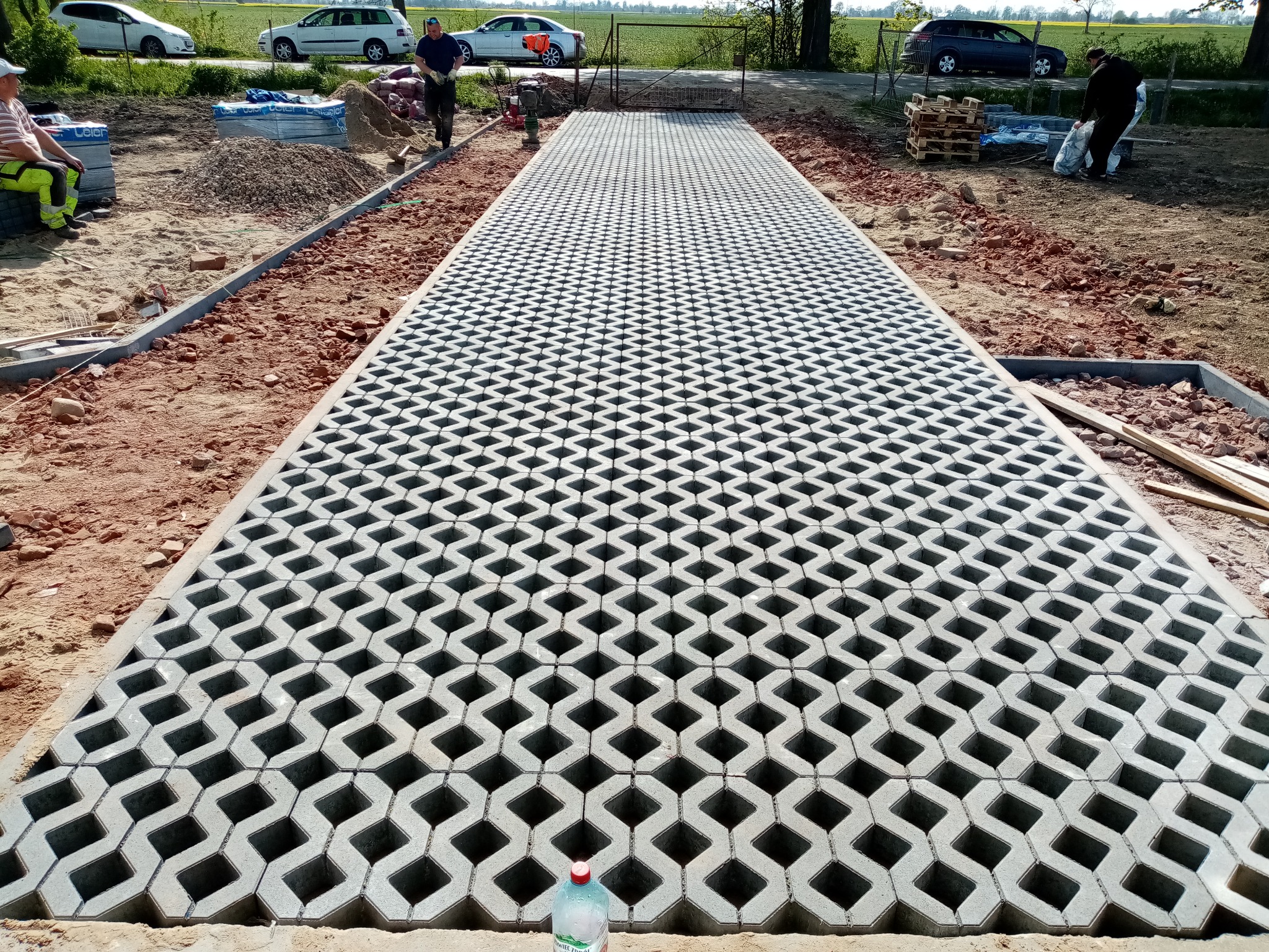 Układanie ażurowej kostki brukowej w Nowym Dworze Gdańskim. Widok na długi, częściowo ułożony podjazd z kostki, przygotowany pod dalsze prace.