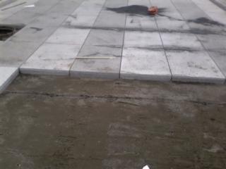 Fragment nowej, szarej nawierzchni ułożonej z płyt betonowych, widoczne nierówności podłoża i pozostałości piasku.