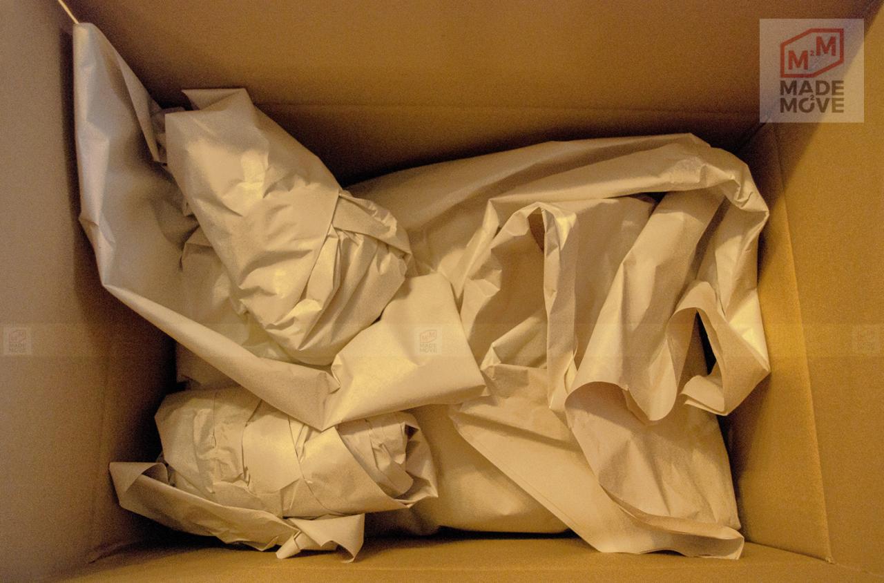 Karton wypełniony papierem pakowym, widoczne logo firmy na ścianie kartonu.