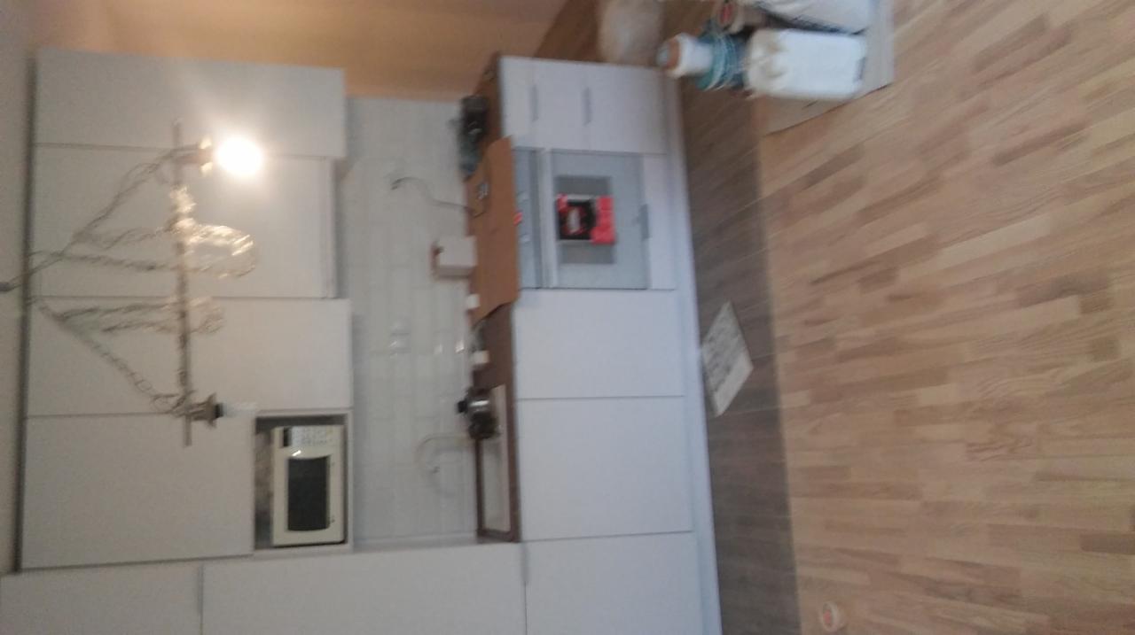 Montaż białej zabudowy kuchennej w trakcie realizacji w Warszawie, widoczne podłączenia elektryczne i fragment drewnianej podłogi.