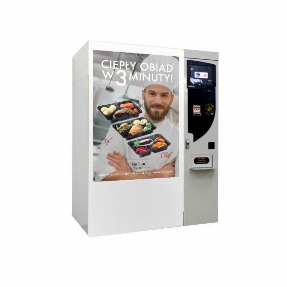 Automat vendingowy z reklamą ciepłych obiadów w 3 minuty, prezentujący uśmiechniętego kucharza i trzy pojemniki z gotowymi daniami.