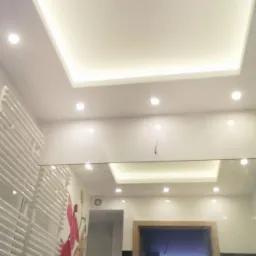 Nowoczesna łazienka z podwieszanym sufitem z oświetleniem LED, grzejnikiem drabinkowym i lustrem odbijającym drzwi do innego pomieszczenia, z dekoracyjną naklejką na ścianie przedstawiającą kwiaty.