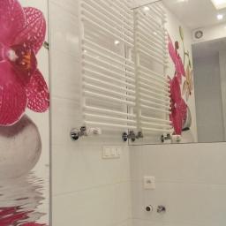 Kompleksowe-Remonty.pl - Biała łazienka z grzejnikiem drabinkowym, płytkami i dużym lustrem, dekorowana motywem kwiatowym na ścianie.