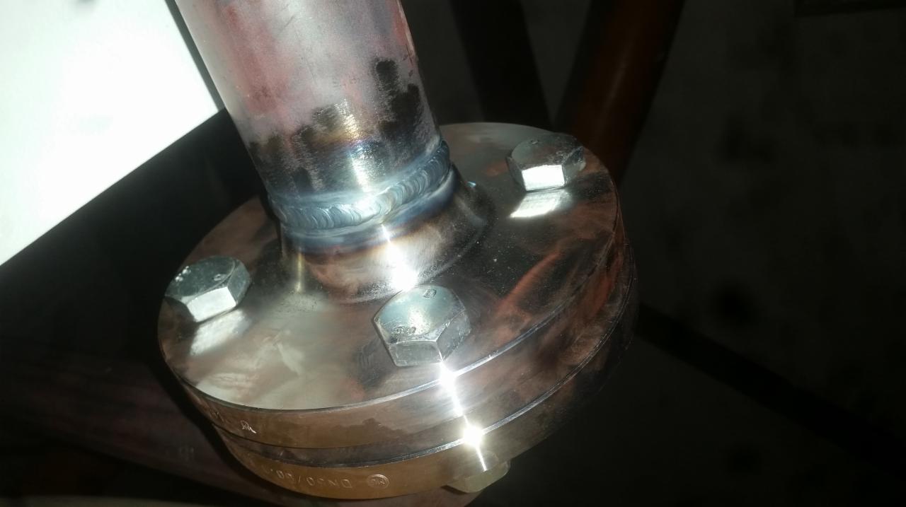 Spoina łącząca rurę ze stalową flanszą, widoczne ślady spawania i śruby mocujące.