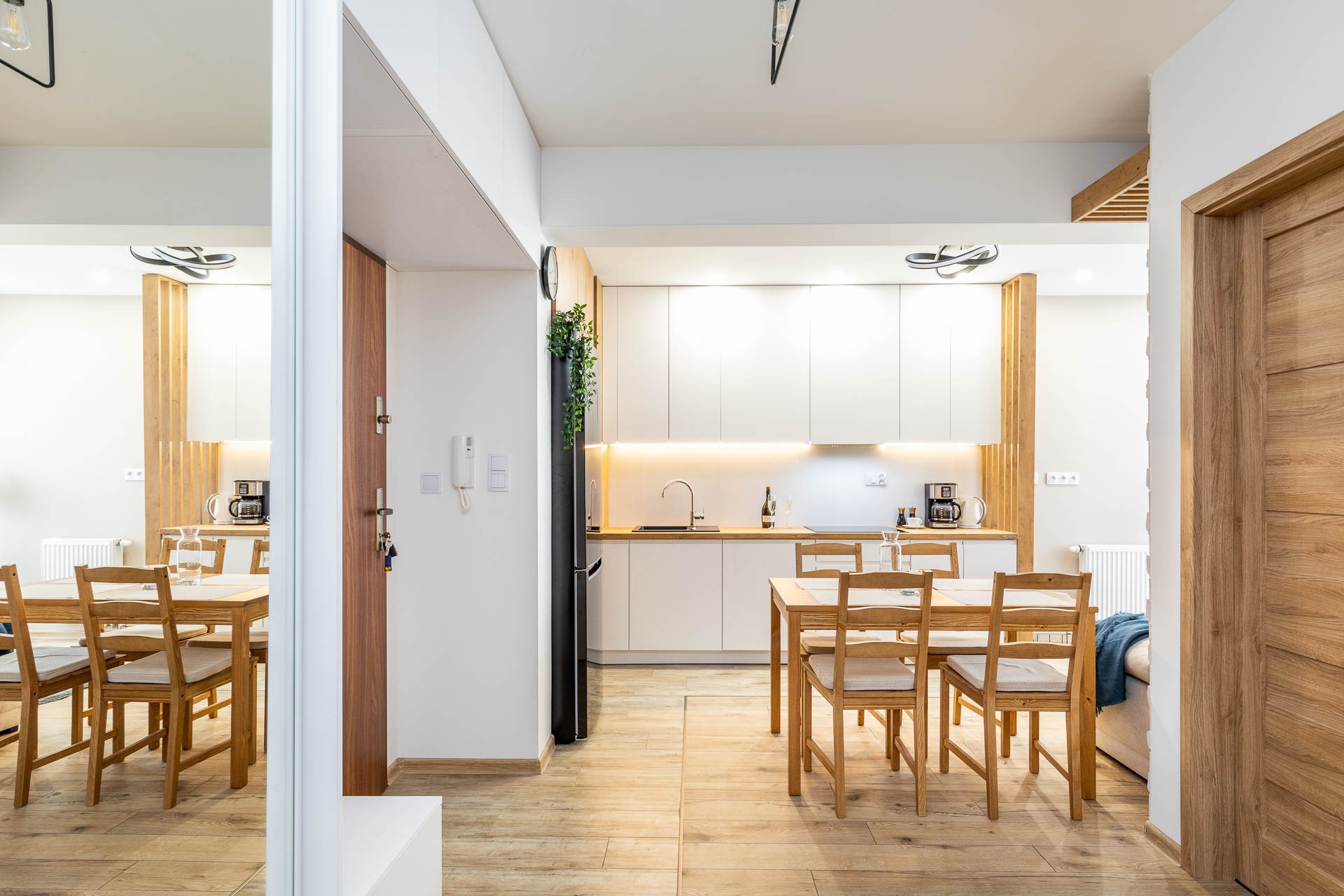 Jasna, nowoczesna kuchnia z drewnianym blatem i stołem w Rudniku, widok z perspektywy wejścia, z lustrzanym odbiciem części jadalni.