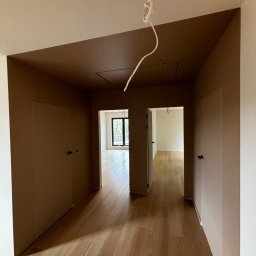 FinitoHome - Pomieszczenie po remoncie: brązowe ściany i sufit, drewniana podłoga, białe listwy przypodłogowe, dwoje drzwi. Widok na jasne pokoje w głębi.