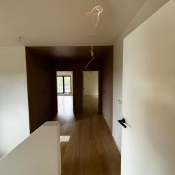 FinitoHome - Korytarz w domu po remoncie. Widoczne świeżo pomalowane ściany w odcieniach bieli i brązu, drewniana podłoga i wiszące kable. Minimalistyczny design.