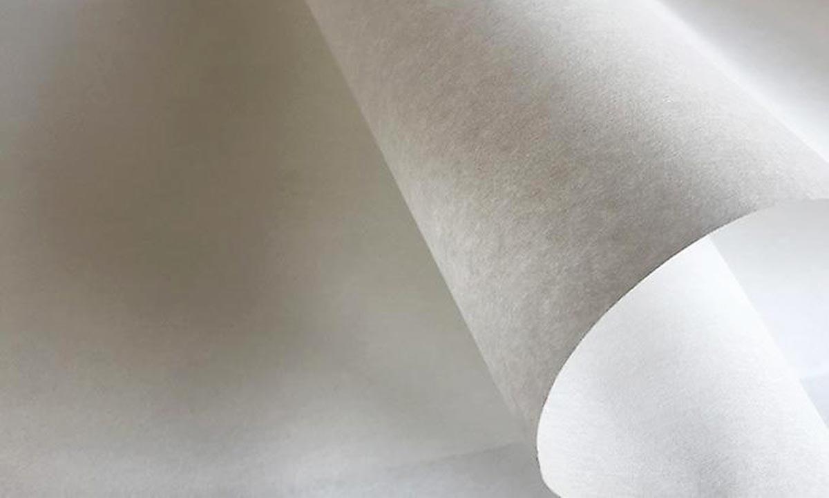 Rolka białej, matowej włókniny o nieregularnej fakturze, częściowo rozwinięta, z widocznymi warstwami.