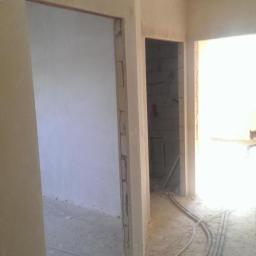 Werbex Sp z o.o. - Wnętrze w stanie surowym: szare ściany, widoczne instalacje elektryczne w peszlach na podłodze, przygotowane otwory na drzwi.