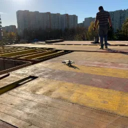 Konstrukcja szalunkowa drewniana przygotowana pod wylanie stropu, w tle budynki mieszkalne i sylwetka pracownika.