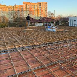 Werbex Sp z o.o. - Siatka zbrojeniowa na przygotowanym podłożu, widoczny pracownik i narzędzia, budynek mieszkalny w tle, pora dnia.