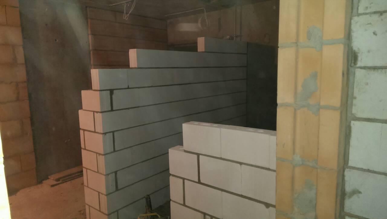Wznoszenie ściany działowej z bloczków betonu komórkowego, widoczny fragment muru z żółtej cegły oraz nieotynkowana ściana w tle.