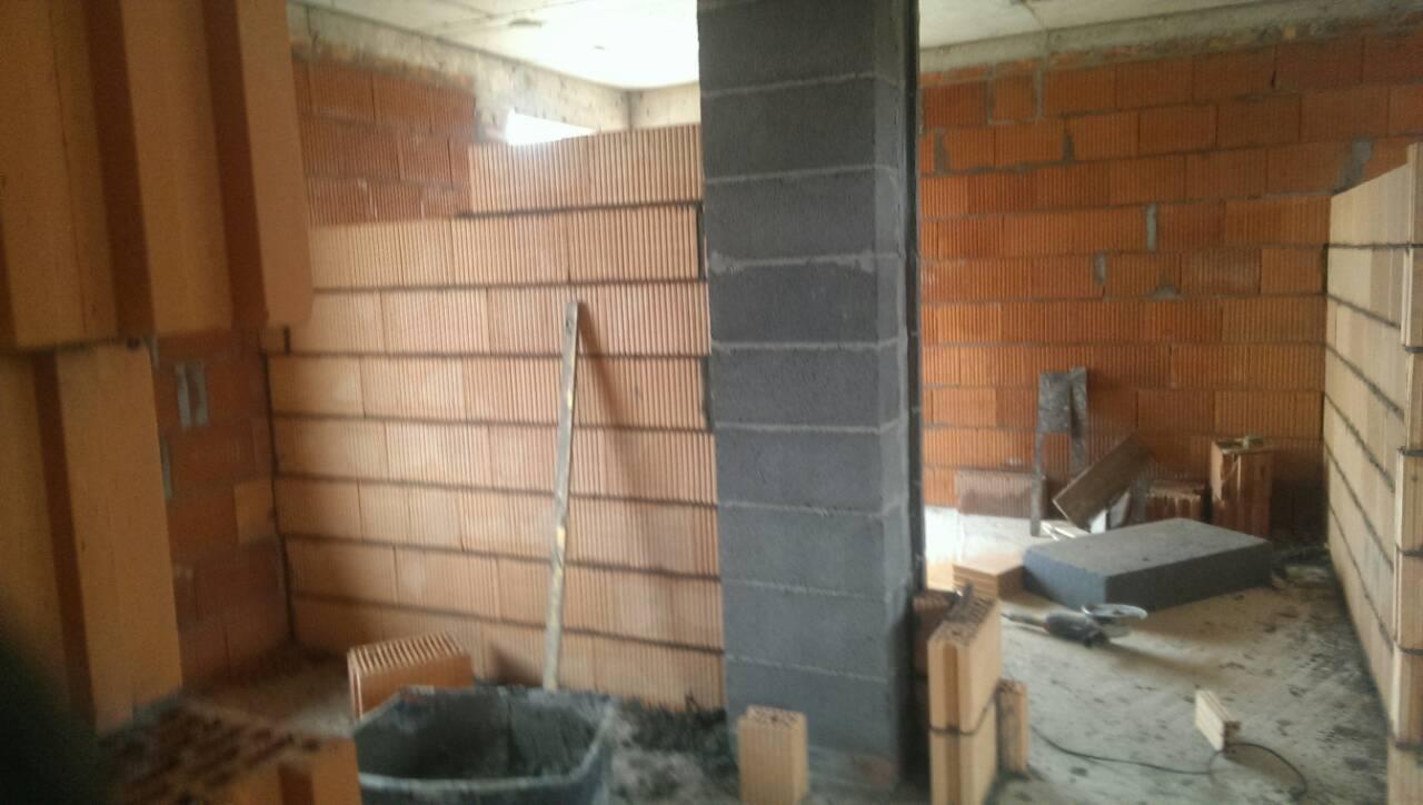 Wnętrze w trakcie budowy: ściany z cegły ceramicznej Porotherm, szary słup z bloczków betonowych, widoczny poziomica i zaprawa w wiadrze.