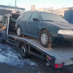 Zielona Skoda Octavia kombi z oszronioną karoserią przewożona na lawecie w zimowych warunkach, widoczny numer rejestracyjny samochodu i lawety.