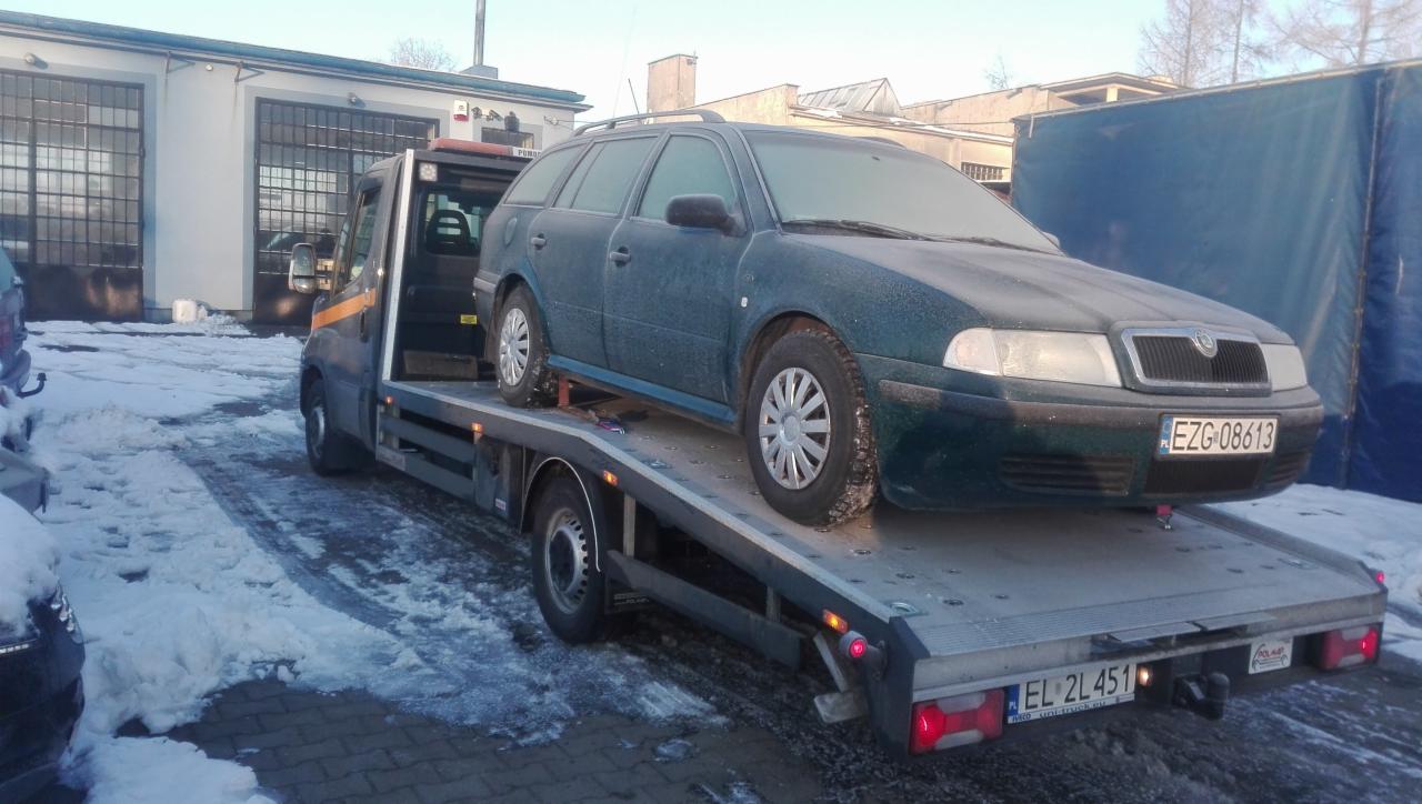 Zielona Skoda Octavia kombi z oszronioną karoserią przewożona na lawecie w zimowych warunkach, widoczny numer rejestracyjny samochodu i lawety.