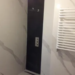 Nowoczesna łazienka z czarną kabiną prysznicową, białą armaturą i marmurowymi płytkami na ścianach i podłodze.