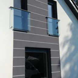 Nowoczesna fasada budynku w Zielonej Górze z dwoma balkonami z szklanymi balustradami, widoczne poziome pasy dekoracyjne na elewacji.