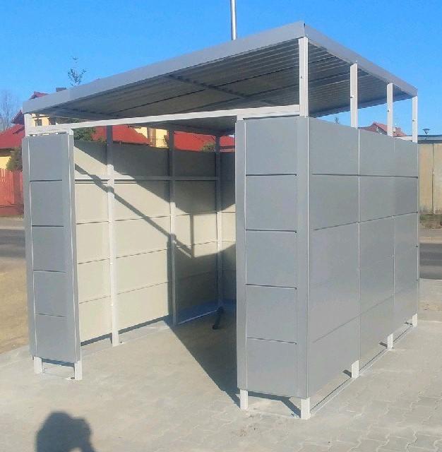 Szara, metalowa konstrukcja zadaszona blachą falistą, prawdopodobnie wiata, na zewnątrz, z widocznymi elementami konstrukcyjnymi i panelami bocznymi.