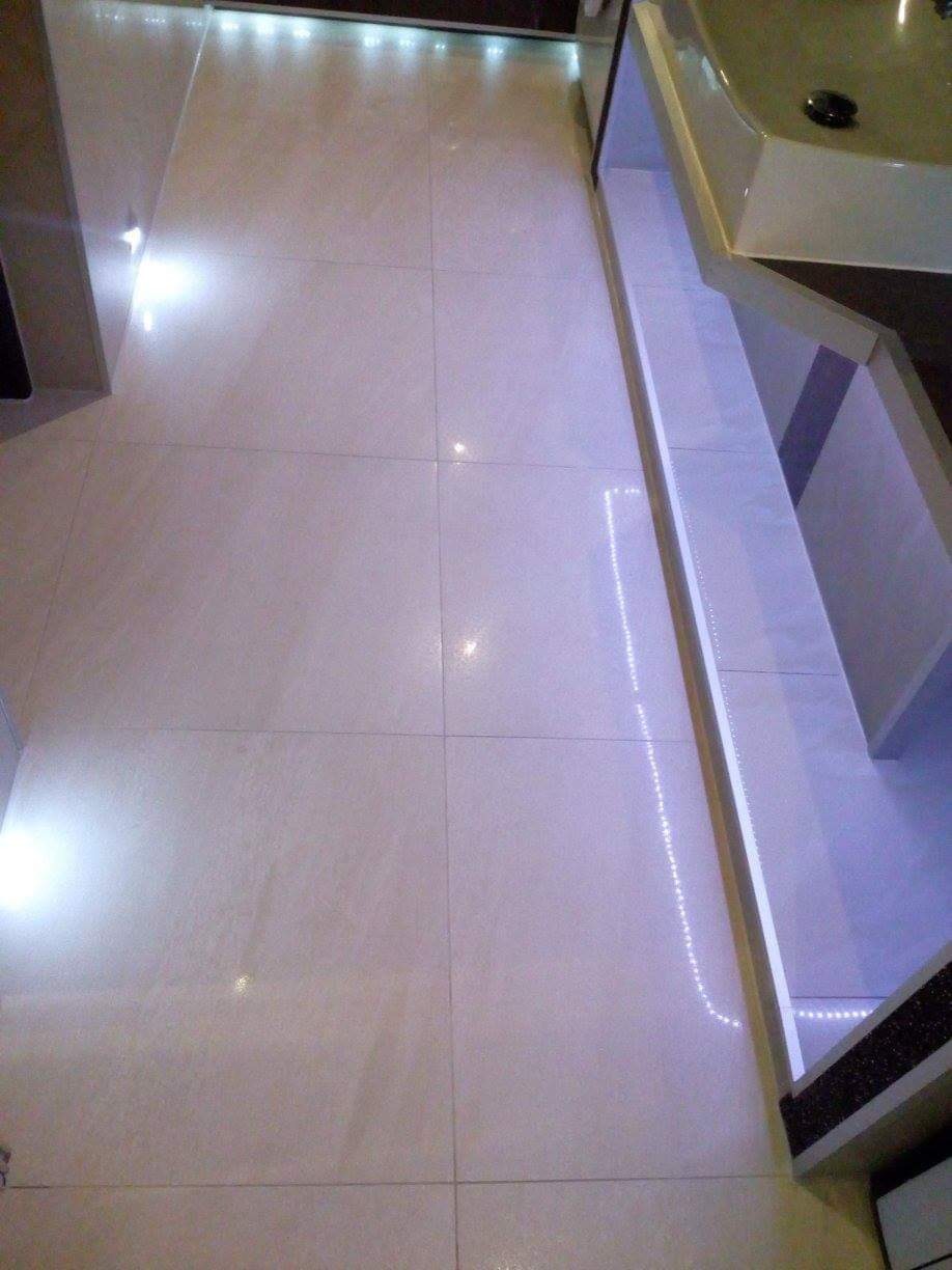 Jasne, błyszczące płytki podłogowe w łazience z oświetleniem LED wzdłuż krawędzi szafki umywalkowej.