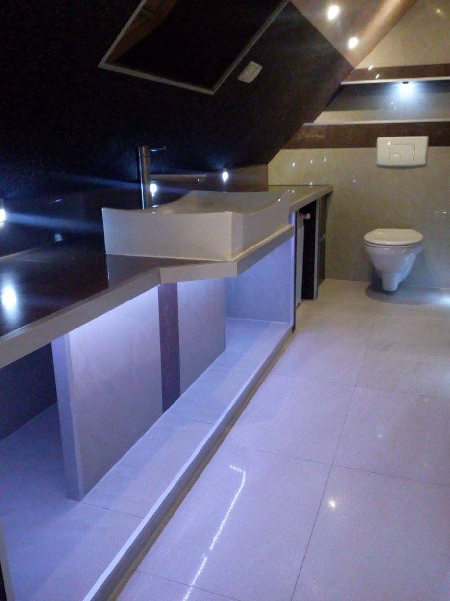 Nowoczesna łazienka z podświetlanym blatem i umywalką nablatową, widoczna toaleta wisząca i płytki w odcieniach szarości i brązu.