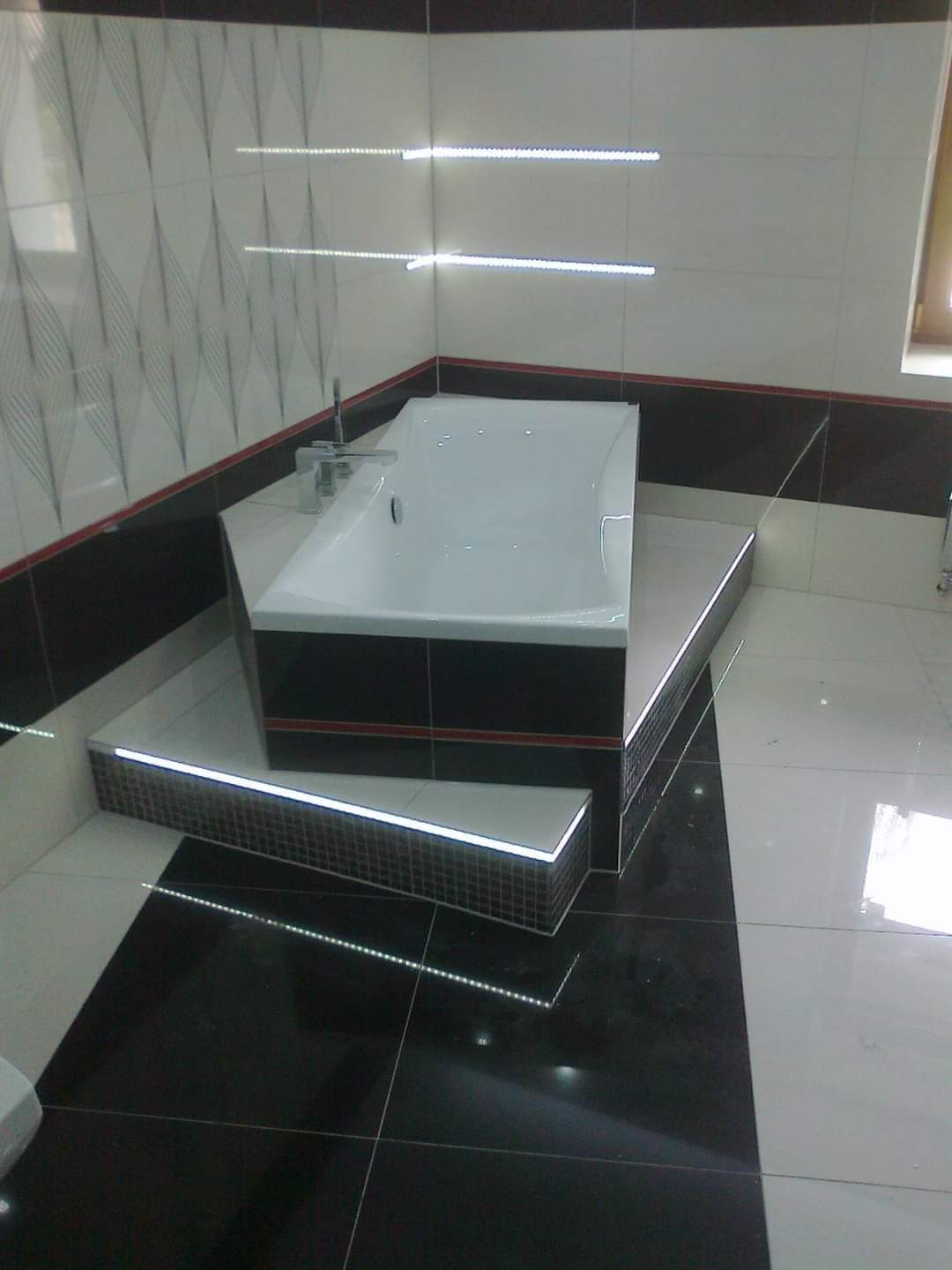 Nowoczesna łazienka z podświetlaną wanną na podeście, czarno-białe płytki, dekoracyjne oświetlenie LED na ścianach.