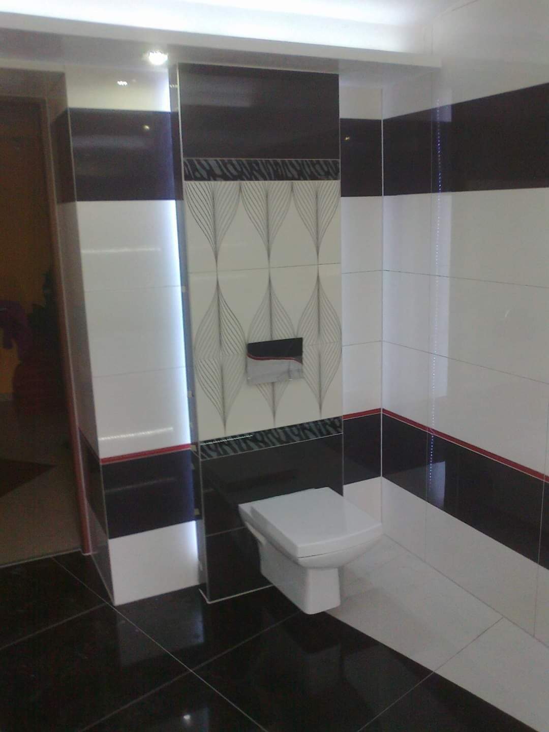 Nowoczesna łazienka z czarno-białymi płytkami, dekoracyjnym wzorem nad toaletą i błyszczącą czarną podłogą.