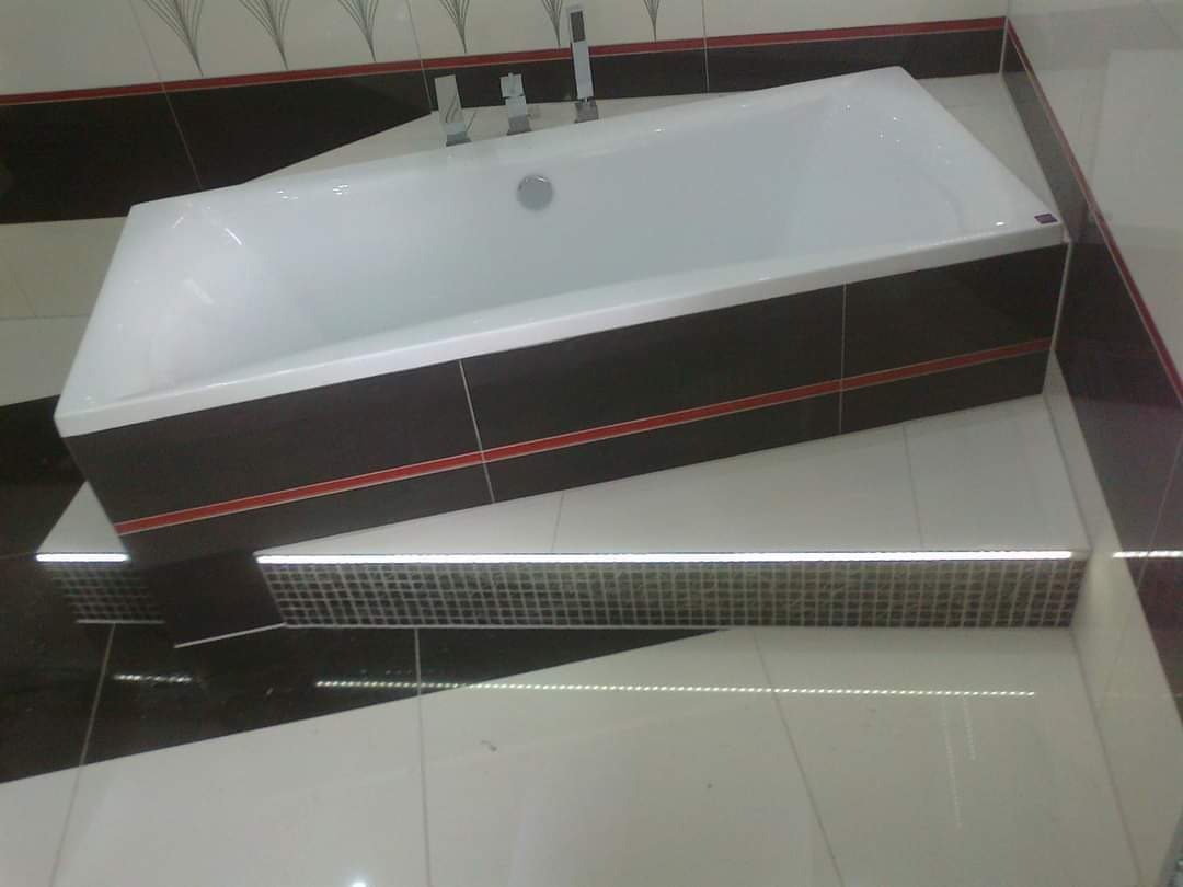 Wanna obudowana ciemnymi płytkami z czerwoną linią, umieszczona na podwyższeniu z mozaiki, biało-czarne płytki podłogowe, wzorzyste płytki ścienne w tle.