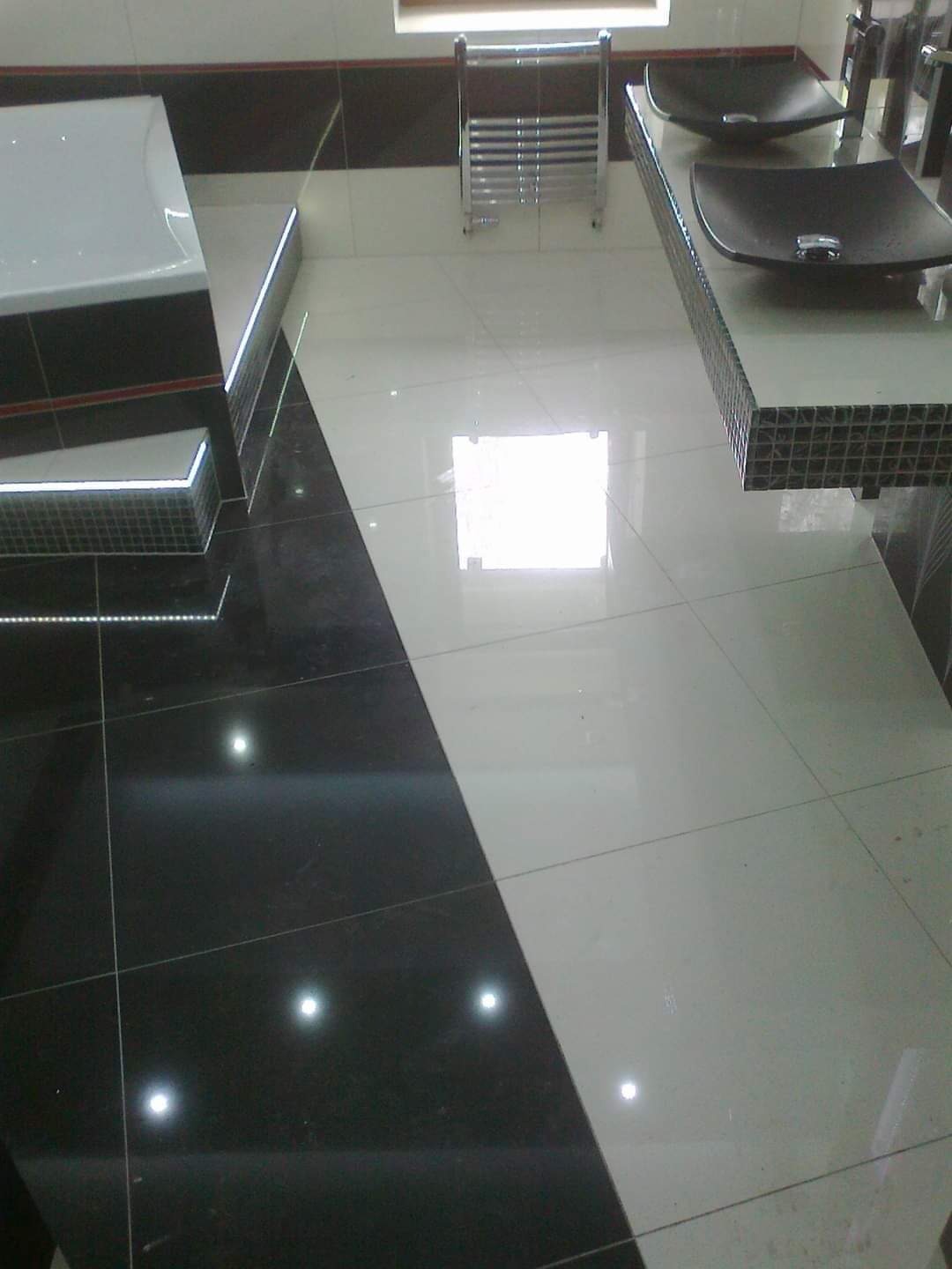 Biało-czarna łazienka z dwoma czarnymi umywalkami nablatowymi, grzejnikiem drabinkowym i podświetleniem LED na obudowie wanny.