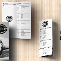 Cztery ulotki reklamowe kawiarni 'TEKTURA bar' z menu, daniami, informacjami kontaktowymi i QR kodami, na drewnianym tle.