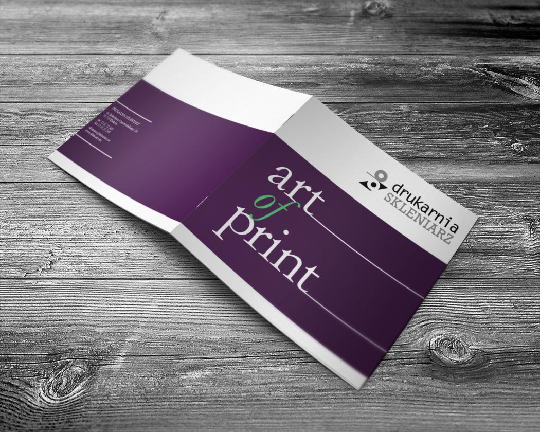 Otwarta, fioletowo-biała broszura reklamowa z tekstem 'art of print' i logo drukarni na tle szarych, drewnianych desek.