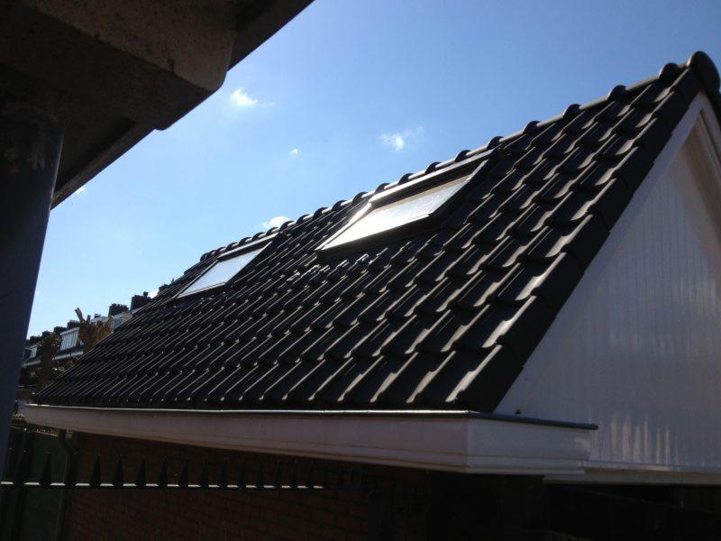 Czarne dachówki z dwoma oknami dachowymi na poddaszu, widok z dołu na tle błękitnego nieba.