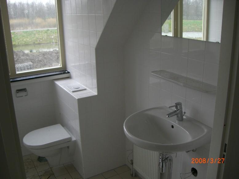 Biała łazienka z toaletą zabudowaną w ścianie, umywalką na szafce z grzejnikiem i oknem z widokiem na zewnątrz, sfotografowana pod kątem.