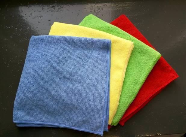 Ułożone kaskadowo, kolorowe ściereczki z mikrofibry: niebieska, żółta, zielona i czerwona, na ciemnej, lekko wilgotnej powierzchni.