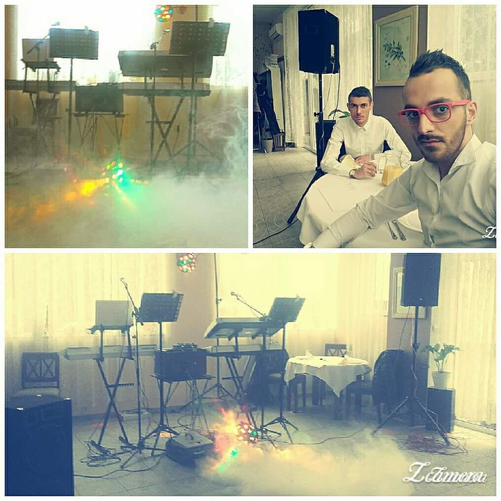 Przygotowany do występu sprzęt muzyczny: keyboardy, mikrofony i oświetlenie sceniczne w zadymionym pomieszczeniu, z widocznymi stolikami i dwoma mężczyznami przy jednym z nich.