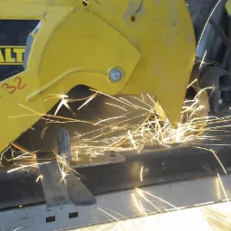 Żółta przecinarka do metalu DeWalt w akcji, z iskrami rozbryzgującymi się podczas cięcia metalowego profilu.