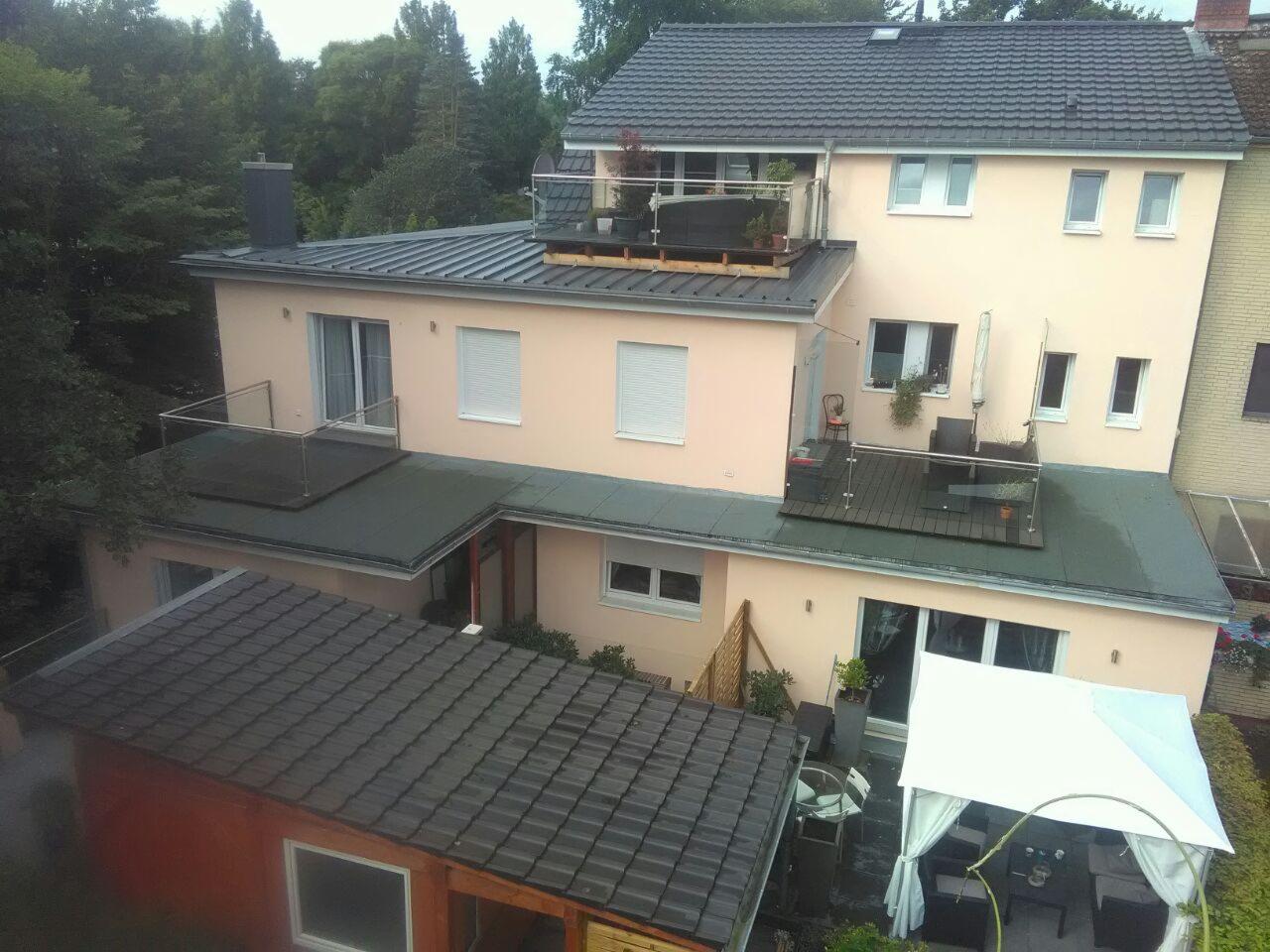 Widok z góry na dwukondygnacyjny dom z płaskim i skośnym dachem, z balkonami z przeszklonymi balustradami i meblami ogrodowymi, oraz altaną w ogrodzie.