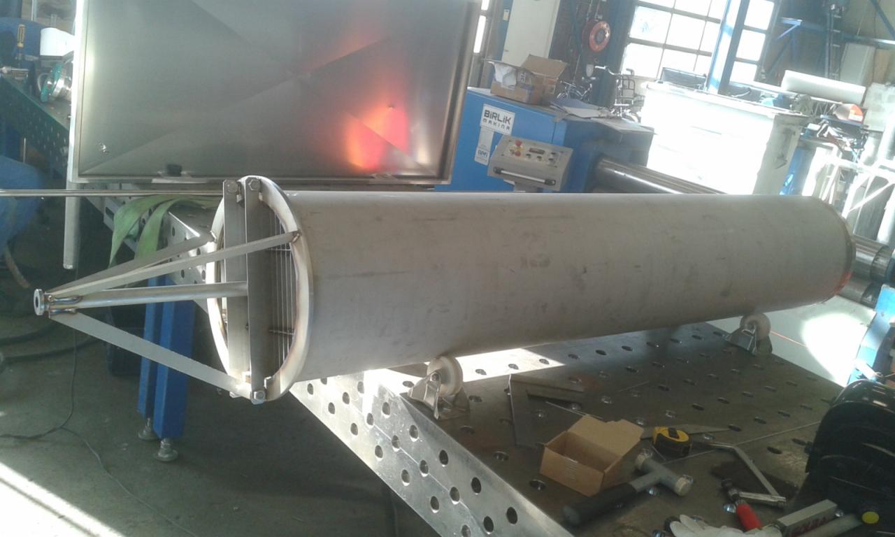 Cylindryczny element konstrukcyjny ze stali nierdzewnej z wewnętrzną kratownicą, umieszczony na perforowanym stole warsztatowym w hali produkcyjnej.