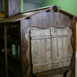 Drewniana konstrukcja przypominająca domek z okiennicami i kominem, wykonana z ciemnego, bejcowanego drewna, z dekoracyjnymi wykończeniami i półkami widocznymi z boku, ustawiona w pomieszczeniu...