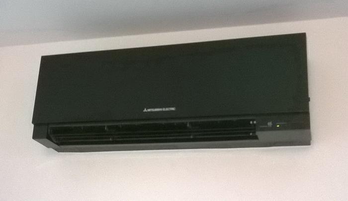 Czarna jednostka wewnętrzna klimatyzatora Mitsubishi Electric zamontowana na białej ścianie, widoczna dioda sygnalizacyjna.