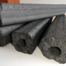 Cztery brykiety węglowe o cylindrycznym kształcie z widocznymi porami i wgłębieniami, ułożone na białym tle z delikatnym oświetleniem.